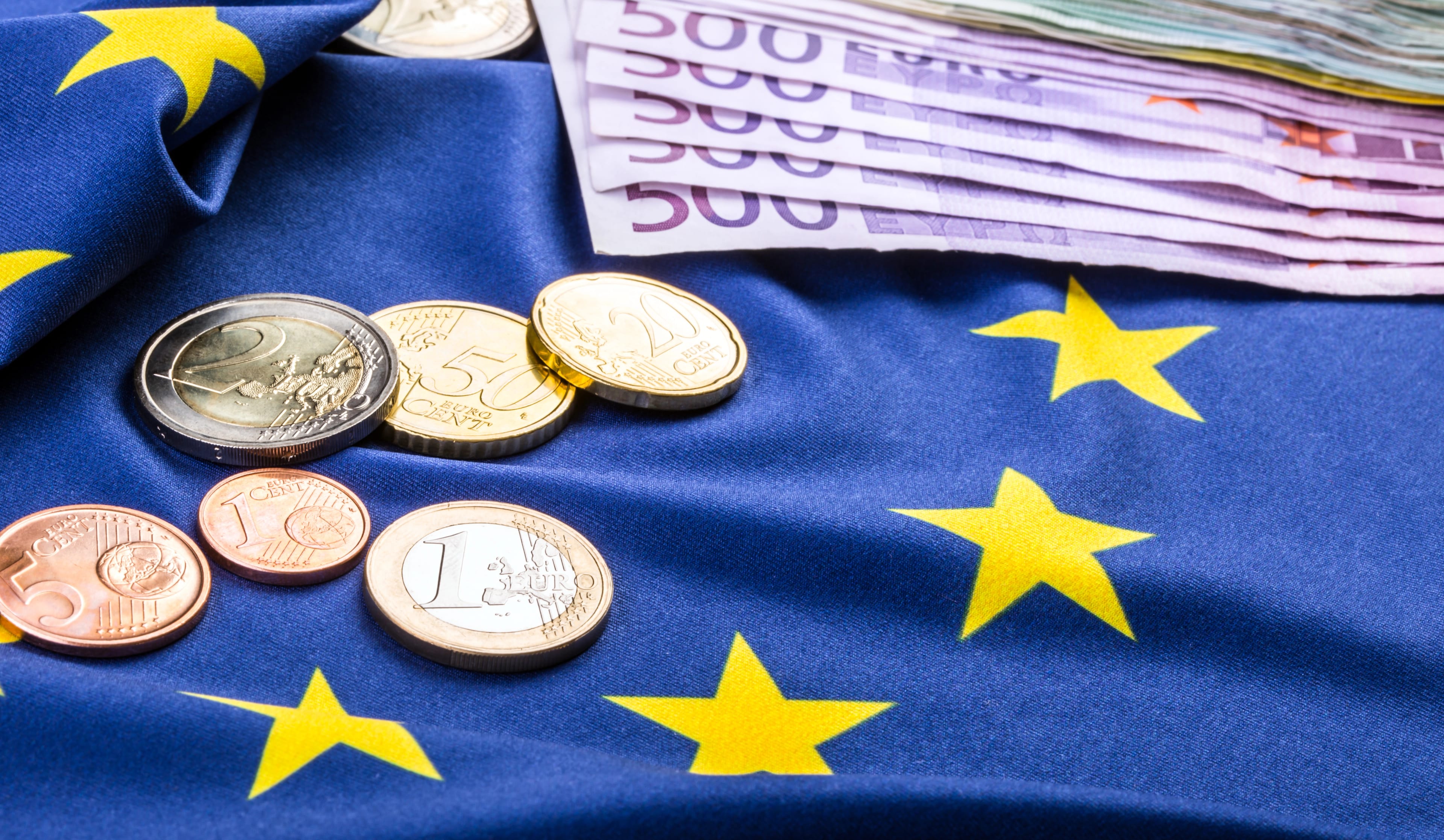 Euro,Coins,And,Banknotes,Freely,Laid,On,The,European,Flag.